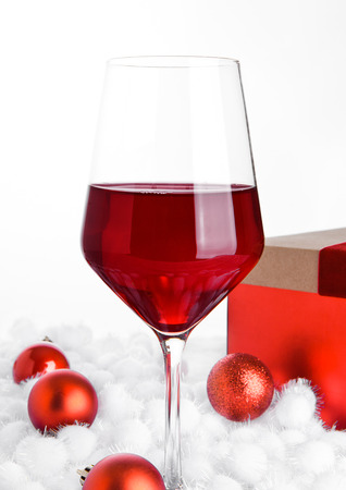Glass of red wine on snow with christmas balls on white backgroundの写真素材