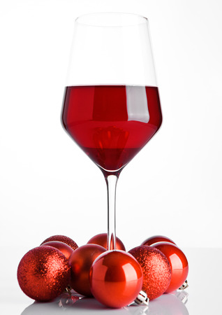 Glass of red wine on snow with christmas balls on white backgroundの写真素材
