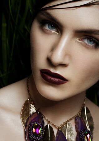 Beautiful woman wearing exotic tropical jewelry on green plants backgroundの写真素材