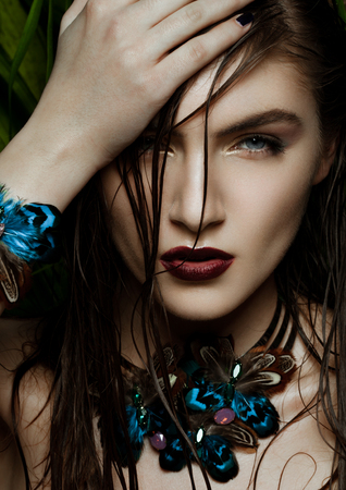 Beautiful woman wearing exotic tropical jewelry on green plants backgroundの写真素材