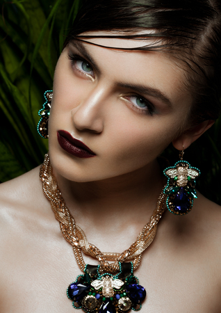 Beautiful woman wearing exotic tropical jewelry on green plants backgroundの写真素材
