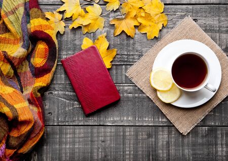 Cup of tea with lemon with scarf and autumn leaves on wooden backgroundの写真素材