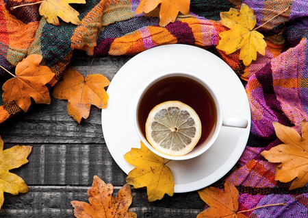 Cup of tea with lemon with scarf and autumn leaves on wooden backgroundの写真素材