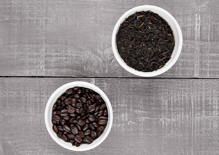 Coffee beans and loose tea in white bowls on wooden backgroundの写真素材