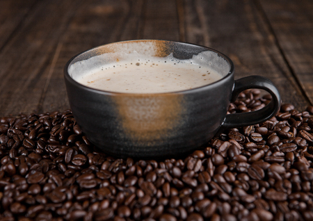 Large cup with hot cappuccino with coffee beans on wooden boardの写真素材