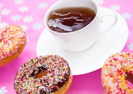 Cup of tea for breakfast with donuts in motion on pink snowflakes backgroundの写真素材