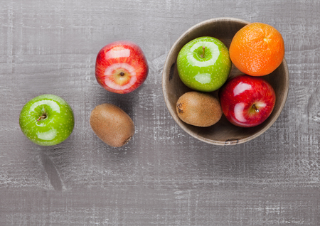 Apples with kiwi and orange in wooden bowl on tableの写真素材