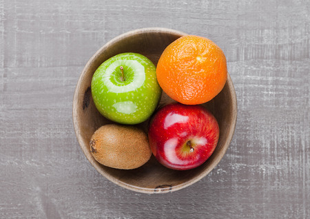 Apples with kiwi and orange in wooden bowl on tableの写真素材