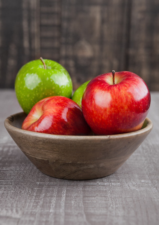 Red and green apples in wooden bowl on wooden boardの写真素材