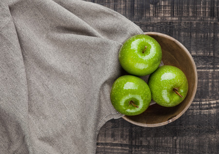 Green healthy apples in wooden bowl kitchen cloth on wooden backgroundの写真素材