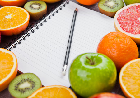 Fruits mix grapefruit orange apples with notebook on wooden backgroundの写真素材