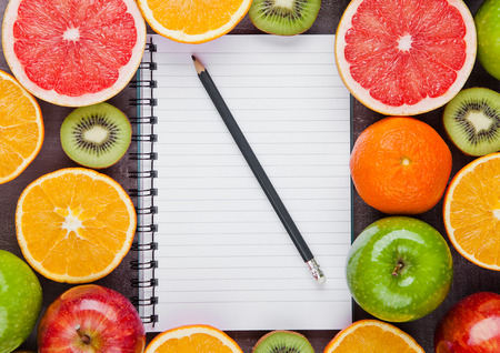 Fruits mix grapefruit orange apples with notebook on wooden backgroundの写真素材