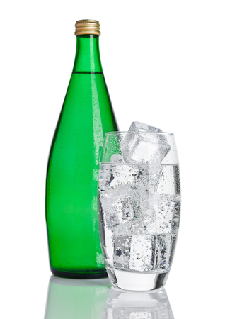 Bottle and glass with healthy sparkling  water with ice cubes on whiteの写真素材