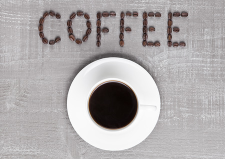 Cup of fresh coffee with sign made from beans on wooden background for cafeの写真素材