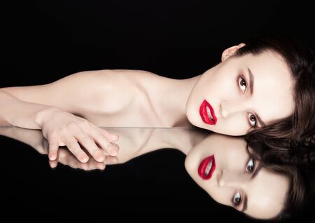 Beauty makeup fashion model with red lips and hand on mirror reflection black backgroundの写真素材