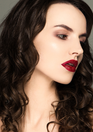Beauty red lips makeup fashion model curly hair on grey background in warm tonesの写真素材