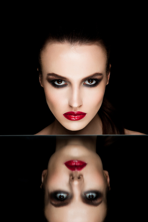 Beauty makeup fashion model with red lips and hand on mirror reflection black backgroundの写真素材