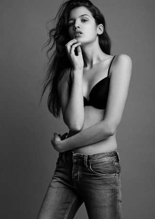 Model test portrait with young beautiful fashion model posing on grey background. Black bra and jeansの写真素材
