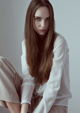 Model test with young beautiful fashion model with long hair wearing white shirt on grey backgroundの写真素材