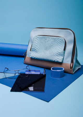 Blue color fashion style still life setup on blue background with bag glasses and penの写真素材