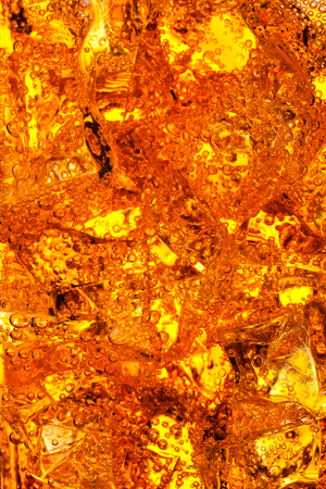 Orange energy soda drink in glass with ice cubes and bubbles macro の写真素材