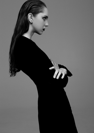 Fashion model with wet hair wearing black long coat on grey background. Fashion portrait. Black and Whiteの写真素材