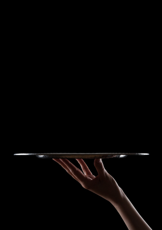 Female hand holds stainless steel catering tray on black background with shadowsの写真素材