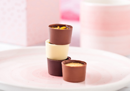 Assortment of luxury white and dark chocolate candies variety on pink plate with cup and gift boxの写真素材