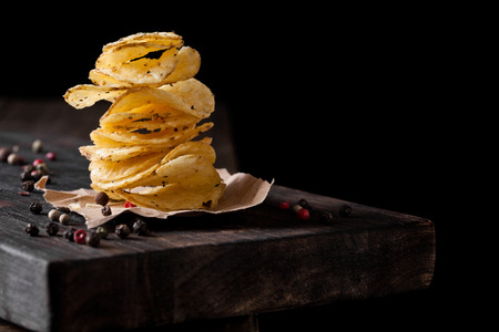 Crispy delicious pepper potato crisps chips snack on dark wooden board and brown paperの写真素材