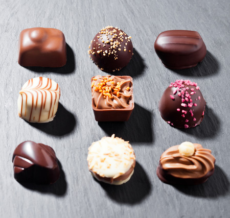 Assortment of luxury white and dark chocolate candies variety on black stone background with hard shadowsの写真素材
