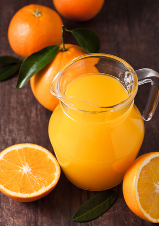 Glass jar of organic fresh orange juice with raw oranges on dark wooden backgroundの写真素材