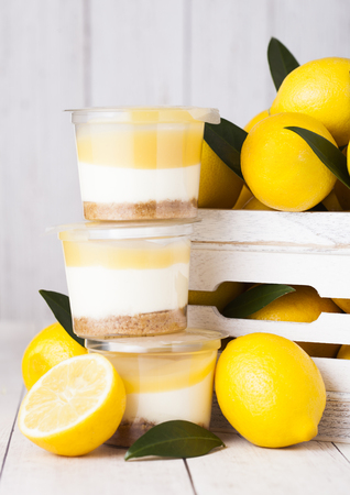 Plastic cup with lemon cream and biscuit dessert with raw lemons in white wooden boxの写真素材