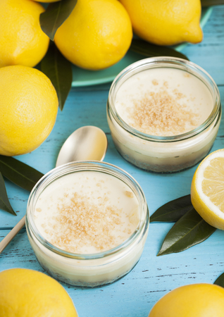 Glass jar with lemon cheesecake with fresh lemons on bluw wooden backgroundの写真素材