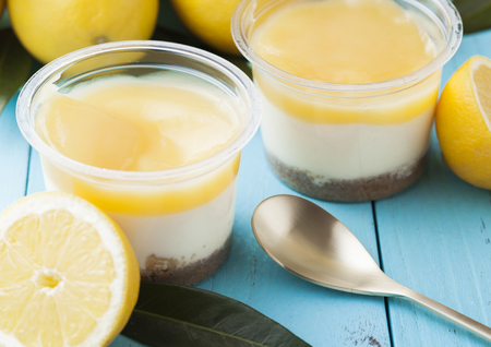 Plastic cups with lemon cream and biscuit dessert with raw lemons on blue wooden background.Top viewの写真素材