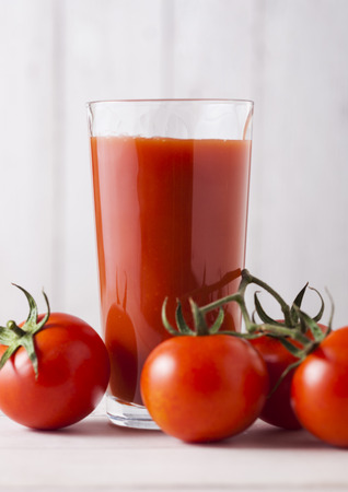 Glass of fresh organic tomato juice with raw tomatoes on light wooden backgroundの写真素材