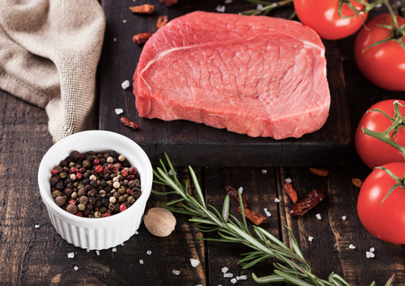 Fresh raw beef steak meat on wooden kitchen board with tomatoes and pepperの写真素材