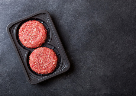 Plastic tray with raw minced homemade grill beef burgers with spices and herbs. Top view and space for text on stone kitchen table backgroundの写真素材