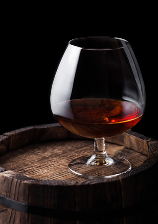 Glass of cognac brandy drink on top of wooden barrel on black background.の写真素材
