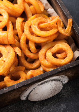 Curly fries fast food snack in wooden box on kitchen background. Unhealthy junk foodの写真素材