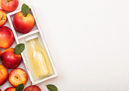 Glass bottle of fresh organic apple juice with red apples in vintage box on wood background.の写真素材