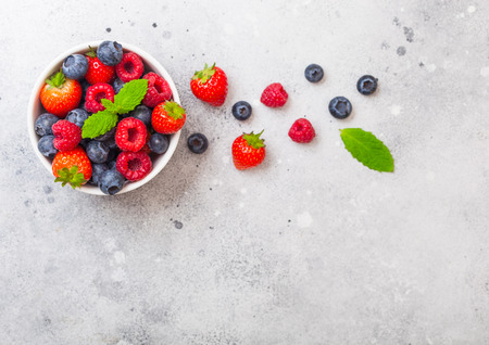 Fresh raw organic berries in white ceramic bowl on kitchen table background. Space for text. Strawberry, Raspberry, Blueberry and Mint leafの写真素材