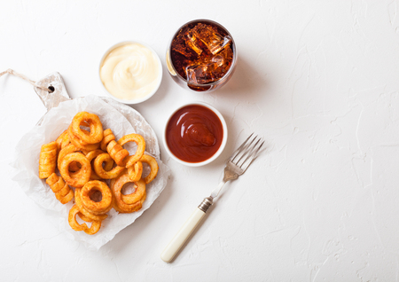 Curly fries fast food snack on wooden board with ketchup and glass of cola on kitchen background. Unhealthy junk foodの写真素材