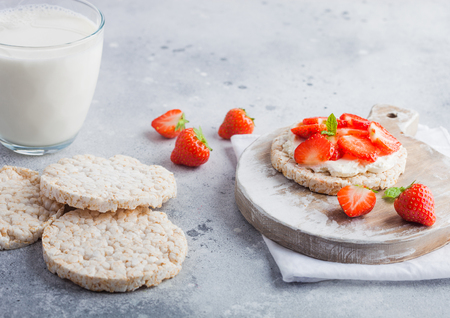 Healthy organic rice cakes with ricotta and fresh strawberries and glass of milk on light stone kitchen background.の写真素材