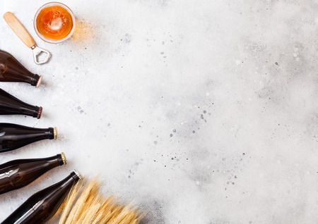 Glass bottles of craft lager beer with raw wheat and opener on stone kitchen table background.の写真素材