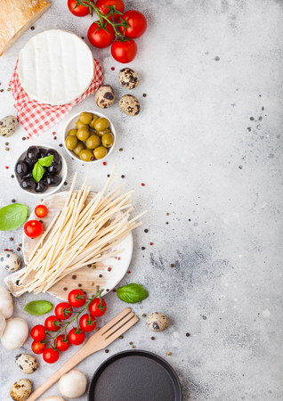 Homemade spaghetti pasta with quail eggs with bottle of tomato sauce and cheese on stone background. Classic italian village food. Garlic, champignons, black and green olives, pan and spatulaの写真素材
