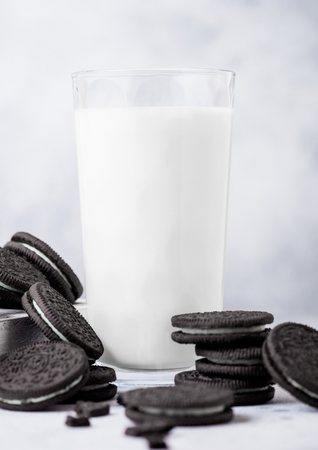 Sandwich black cookie consisting of two chocolate wafers with cream filling with glass of milk on stone board.の写真素材