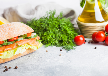 Fresh healthy salmon sandwich with lettuce and cucumber on vintage chopping board on stone background. Breakfast snack. Fresh tomatoes, dill and lemon.の写真素材