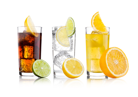 Glasses of cola and orange soda drink and lemonade sparkling water on white background with ice cubes lemons and lime bits