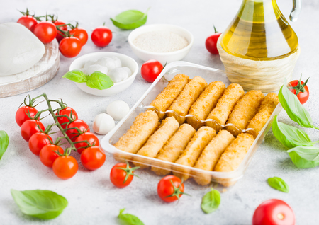 Fresh Mozzarella cheese on vintage chopping board with tomatoes and basil leaf with olive oil and tray with cheese sticks on stone kitchen background.の写真素材