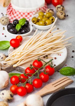 Homemade spaghetti pasta with quail eggs with bottle of tomato sauce and cheese on stone background. Classic italian village food. Garlic, champignons, black and green olives, pan and spatulaの写真素材